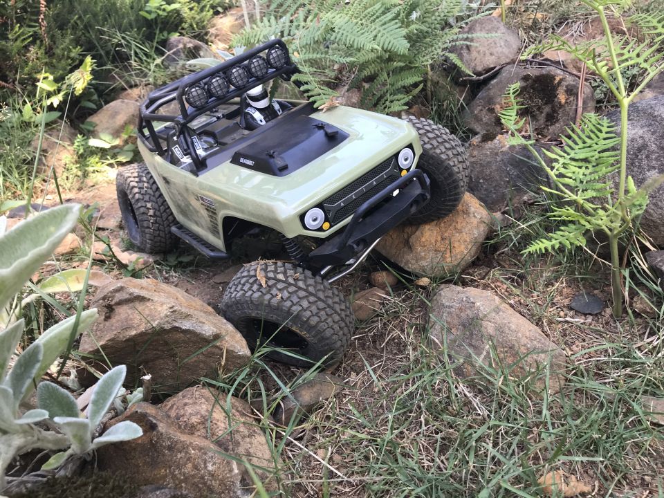 Light green remote-controlled rock crawler with roll cage and lights on rocky terrain.