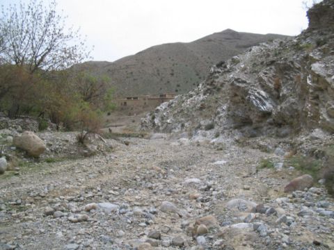 1981 Ford Bronco - A dry riverbed winds through a rocky, mountainous landscape towards a cluster of buildings.