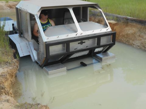 1992 Ford Bronco - A custom-built, amphibious vehicle with a metal body is partially submerged in murky water, with a person in the driver's seat. The vehicle…
