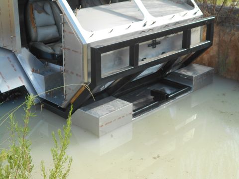 1992 Ford Bronco - A custom-built vehicle, possibly a boat or amphibious vehicle, is partially submerged in murky water. The visible section features unfinish…