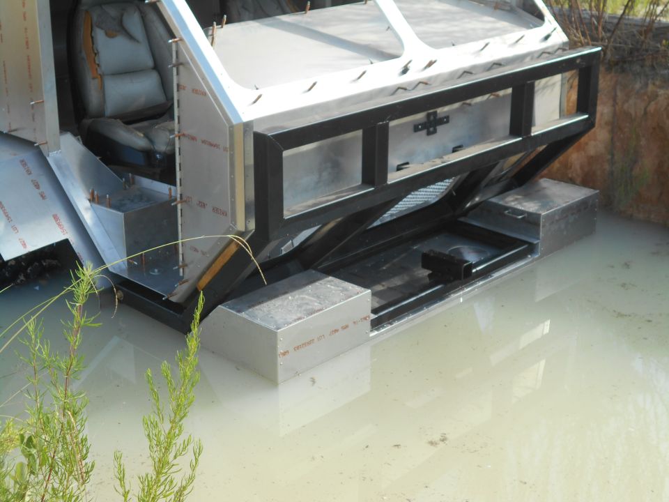 Custom vehicle partially submerged in water, showing unfinished metal construction and a seat.