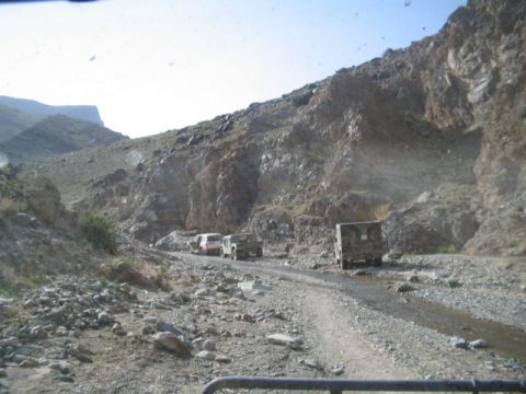 1981 Ford Bronco - A convoy of SUVs and a truck navigates a rough, rocky road through a mountainous terrain.