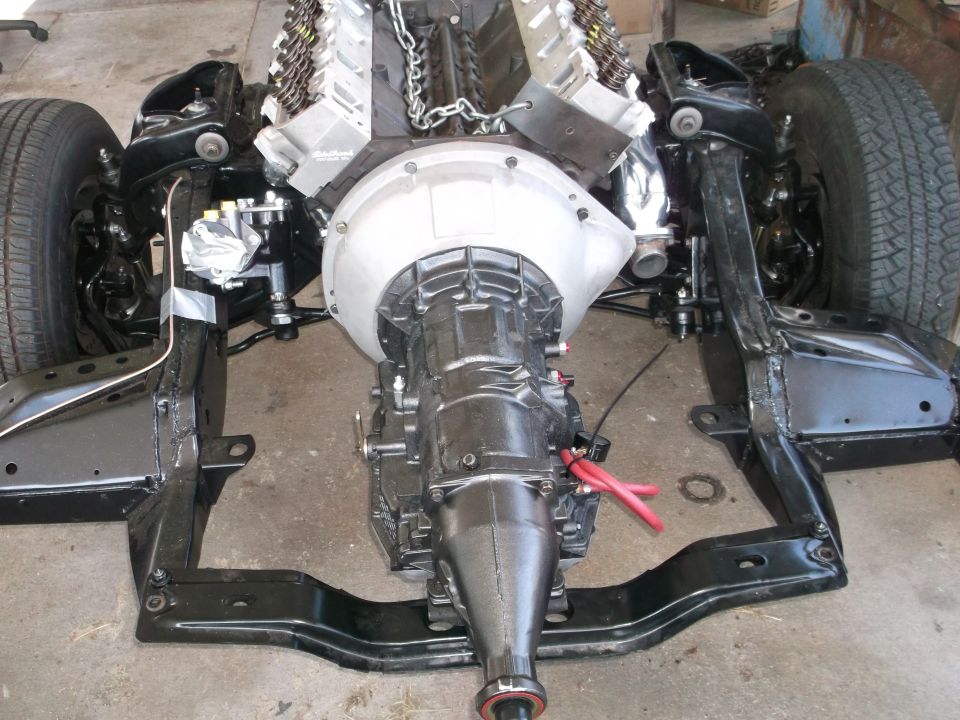 Car frame with V8 engine and transmission installed, top-down view.