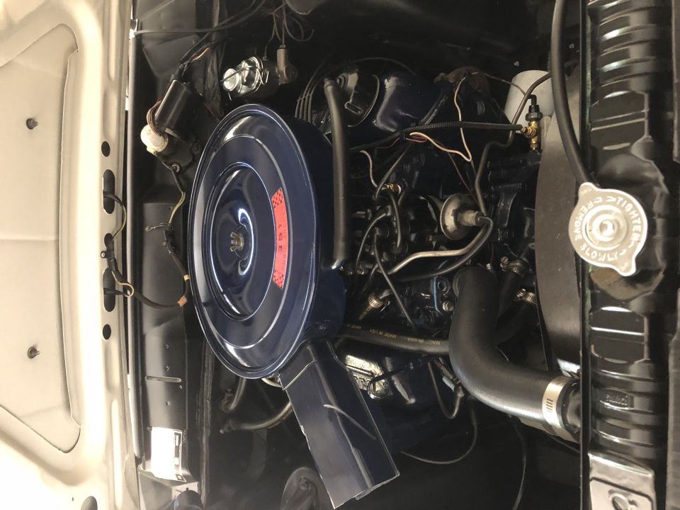 Close-up of a classic car engine bay with blue air cleaner and radiator cap.