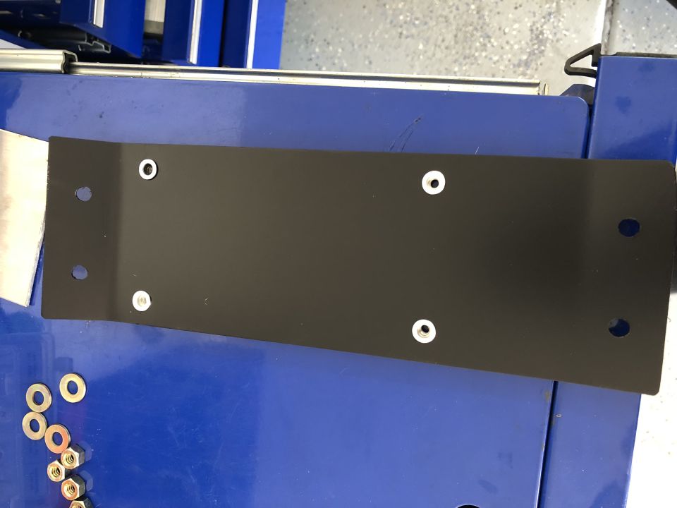 Black metal plate with six holes on a blue surface, with washers and nuts nearby.