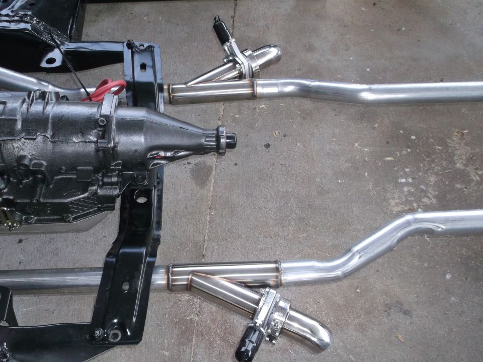 Car chassis with transmission and dual exhaust pipes, on concrete floor