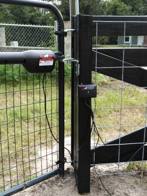 1994 Ford Bronco - An automatic gate opener system is installed on a black metal gate, a warning label on the opener unit.