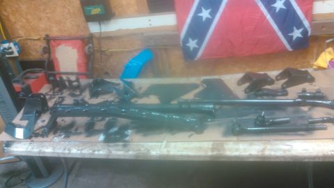 1992 Ford Bronco - Freshly painted gloss-black suspension and steering components laid out to dry on a plywood workbench, including a radius arm, tie rods wit…