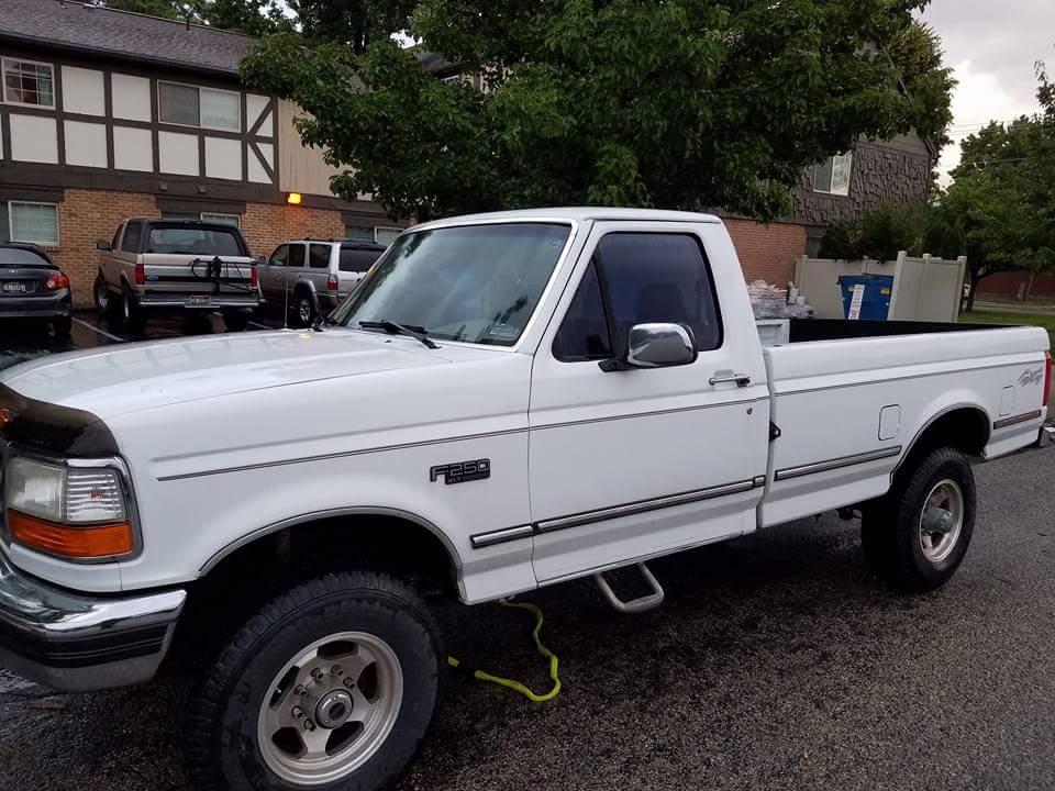 White 1995 Ford F-250 pickup truck parked outside a building, with other vehicles in the background