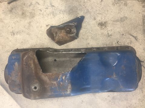 1969 Ford Bronco - A damaged blue oil pan and a separate metal bracket lie on a concrete surface.