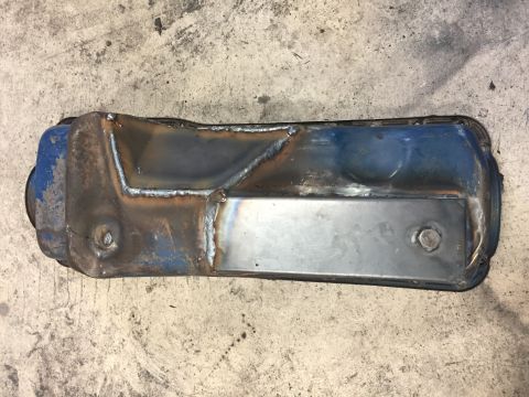 1969 Ford Bronco - Modified valve cover with welded reinforcement plates sits on a concrete floor.
