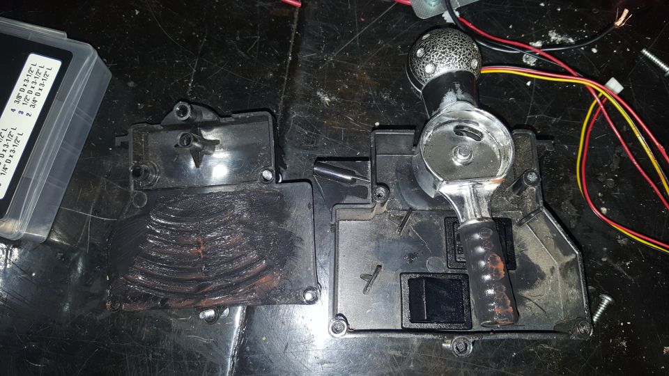 Car gear shifter assembly with wires and a plastic box of parts on a dark surface