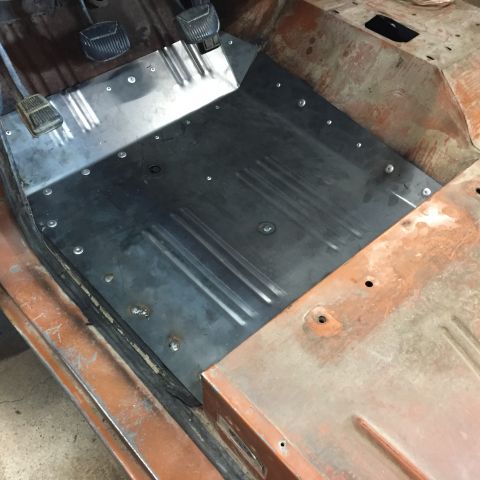 1969 Ford Bronco - New bare-metal floor pan riveted into a vehicle cab next to brake and clutch pedals, surrounded by rusty body.