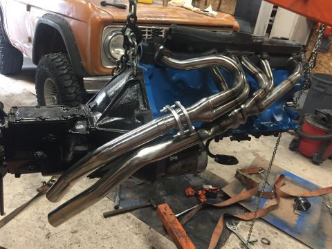 1969 Ford Bronco - Engine and transmission assembly with chrome headers being lowered by chains into a 1969 Ford Bronco.
