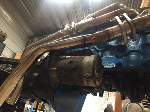 1969 Ford Bronco - Shiny exhaust headers are installed on a blue engine block, with a starter motor visible.
