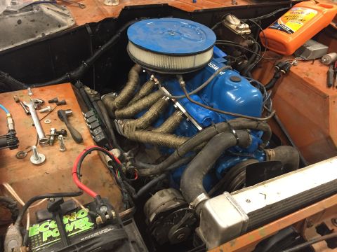 1969 Ford Bronco - Close-up view of an engine bay a blue engine, wrapped exhaust headers, and a battery.