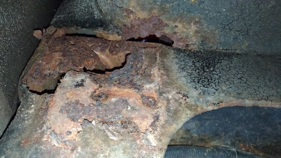 Close-up of heavily rusted metal frame components, possibly from under a vehicle