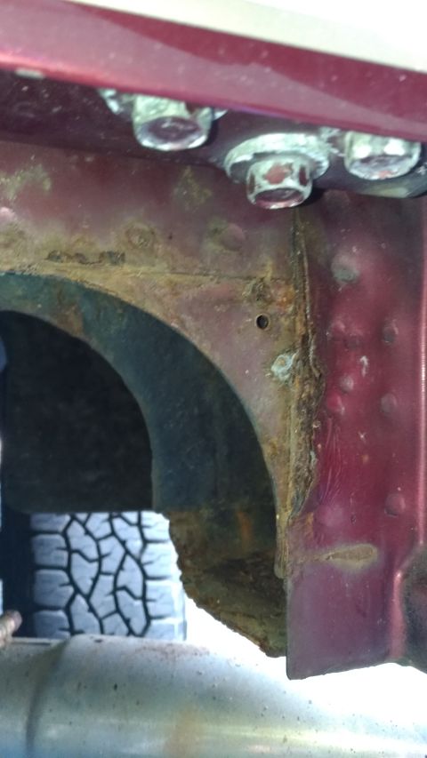 1996 Ford Bronco - Detail of a heavily rusted vehicle frame, showing structural damage and a portion of the tire and exhaust.