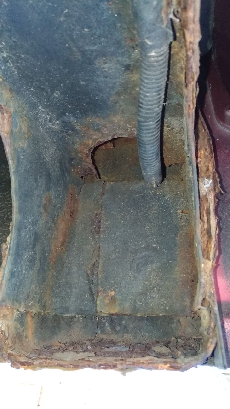 Vehicle frame with extensive rust damage and a black corrugated tube