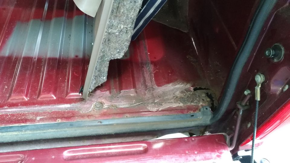 Red vehicle interior showing significant rust damage on the floor panel and surrounding metal