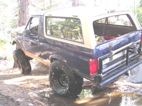 1994 Ford Bronco - This lifted Ford Bronco navigates a rocky, watery trail with an axe mounted on the rear.
