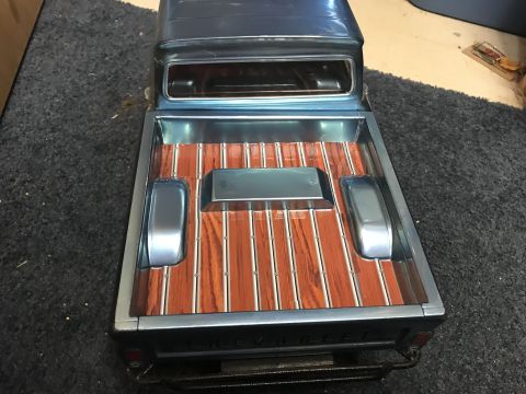 1989 Ford Bronco - The rear view of a blue pickup truck showcases a custom bed with wood-grain flooring and chrome trim.