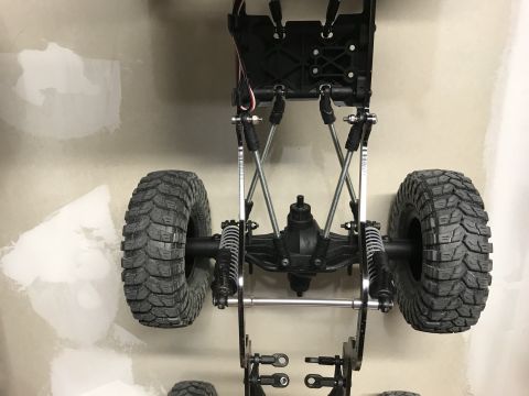 1989 Ford Bronco - The chassis of an RC car, showing its suspension and large tires, is mounted against a wall.