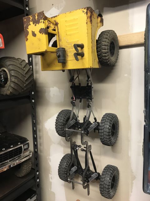 1989 Ford Bronco - RC truck body and chassis assembly hanging on a wall, with another RC vehicle on a shelf below.