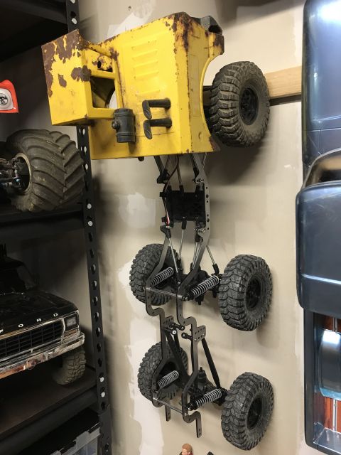 1989 Ford Bronco - A yellow RC truck body is mounted upside down on a wall, showing its chassis and suspension system.
