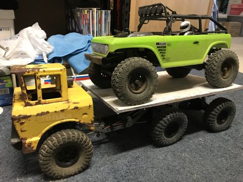 1989 Ford Bronco - A weathered yellow toy truck transports a bright green toy SUV on its flatbed.