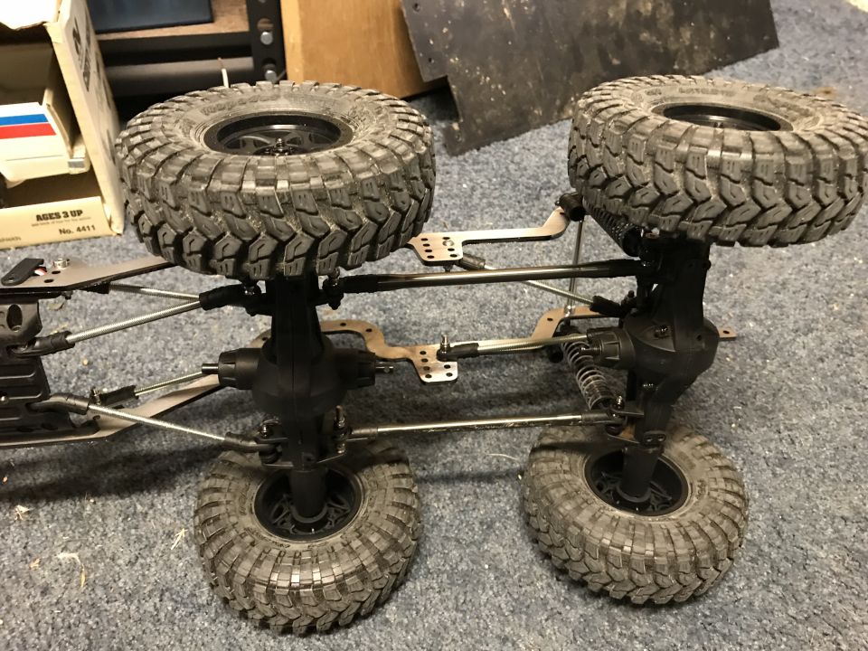 RC car chassis with large off-road tires and suspension components, viewed from below