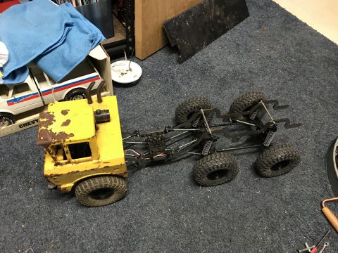 1989 Ford Bronco - A yellow 6x6 truck chassis sits on a carpeted floor, with a toy truck in a box in the background.