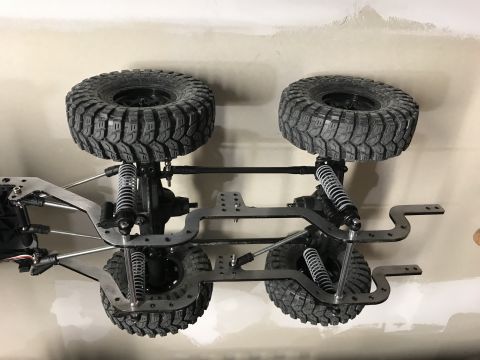 1989 Ford Bronco - The chassis of an RC car, four large tires and visible suspension system, is displayed against a plain wall.