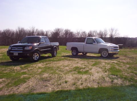 1988 Ford Bronco - Two pickup trucks, a black Toyota and a white Chevrolet, are parked on a grassy field.