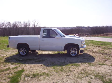 1988 Ford Bronco - A white pickup truck is parked on a dirt lot with trees in the background.