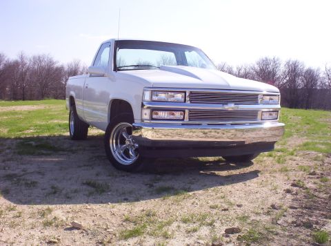 1988 Ford Bronco - A white pickup truck is parked outdoors on a sunny day, showing its front grille and chrome bumper.