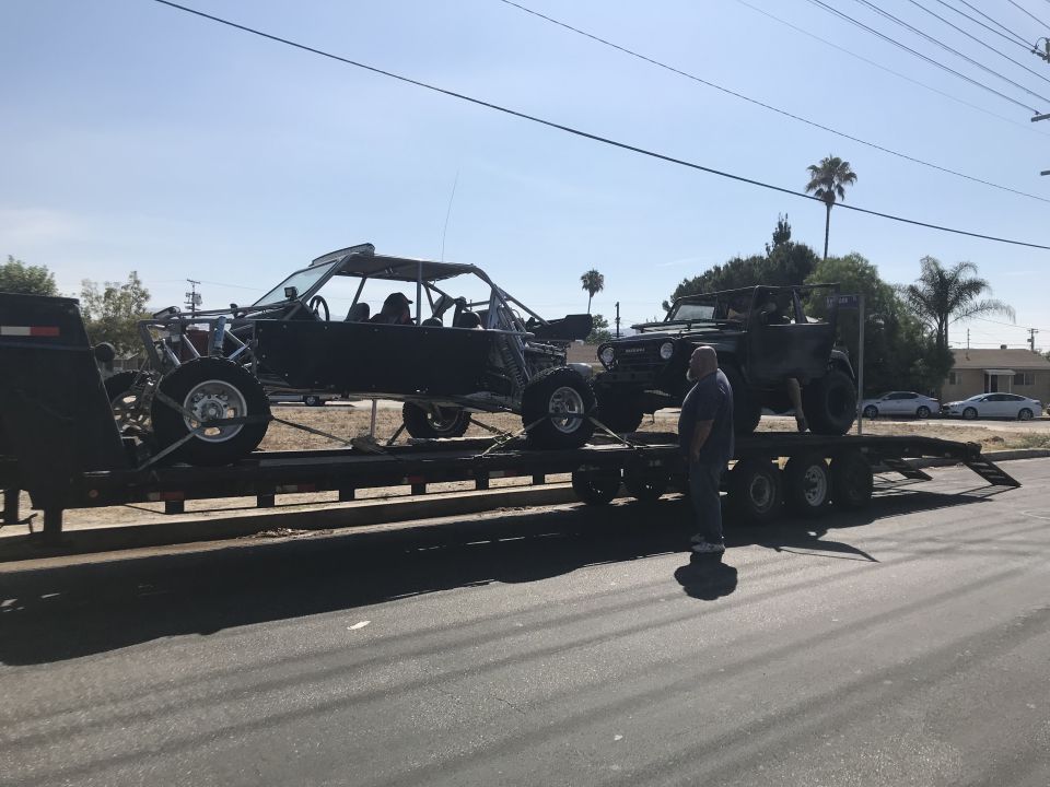 Side view of two off-road vehicles on a trailer, one a dune buggy, the other a Jeep-like vehicle