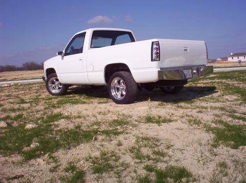 1988 Ford Bronco - White pickup truck with aftermarket chrome wheels seen from the rear quarter angle.