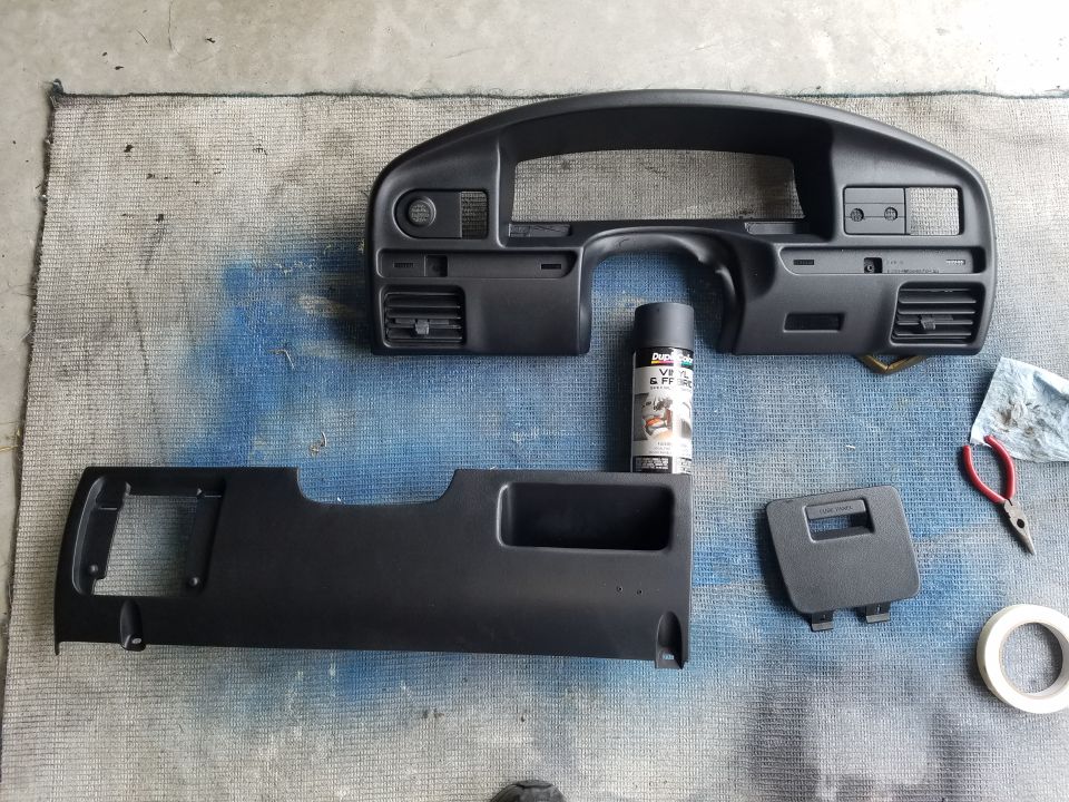 Dashboard trim pieces and a can of black spray paint on a blue drop cloth