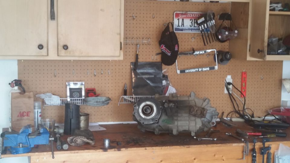Transfer case on a workbench with tools, license plate, and hat on pegboard