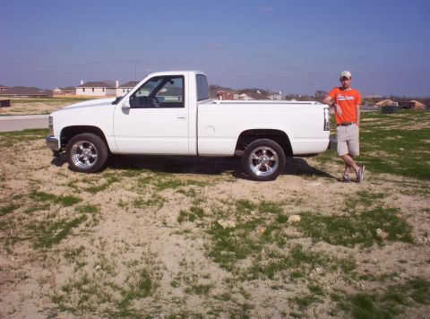 1988 Ford Bronco - A white pickup truck is parked on a dirt lot with a man standing beside it.