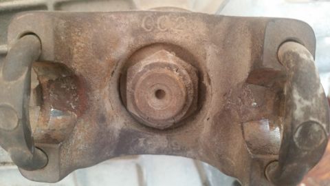 1985 Ford Bronco - This is a close-up view of a rusty driveshaft U-joint, showing some visible markings and a central bolt.