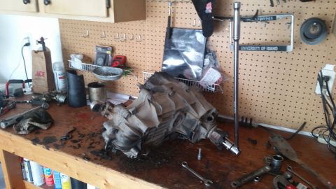 1985 Ford Bronco - A disassembled transmission sits on a workbench, surrounded by various tools and automotive parts.