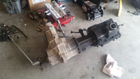 1985 Ford Bronco - Transmission and transfer case assembly resting on a garage floor with tools and equipment in the background.