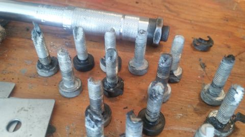 1985 Ford Bronco - Several bolts show signs of damage, lying on a wooden surface next to a torque wrench.
