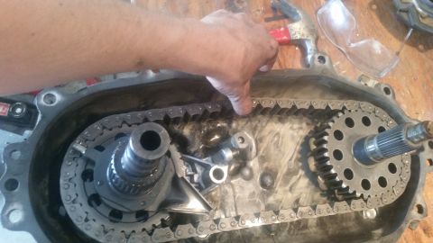 1985 Ford Bronco - Close-up of a transfer case with a hand manipulating the chain and gears.