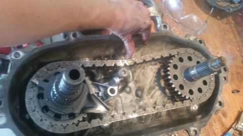 1985 Ford Bronco - A person's hand is shown inside a disassembled transfer case, interacting with the chain and gears.
