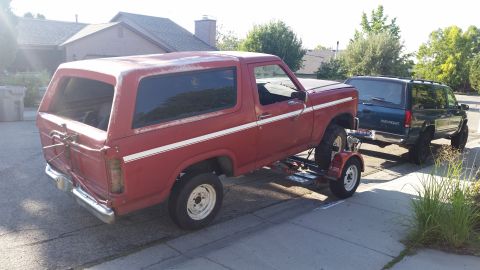 1981 Ford Bronco - A red 1981 Ford Bronco is seen on a trailer, parked next to another SUV.