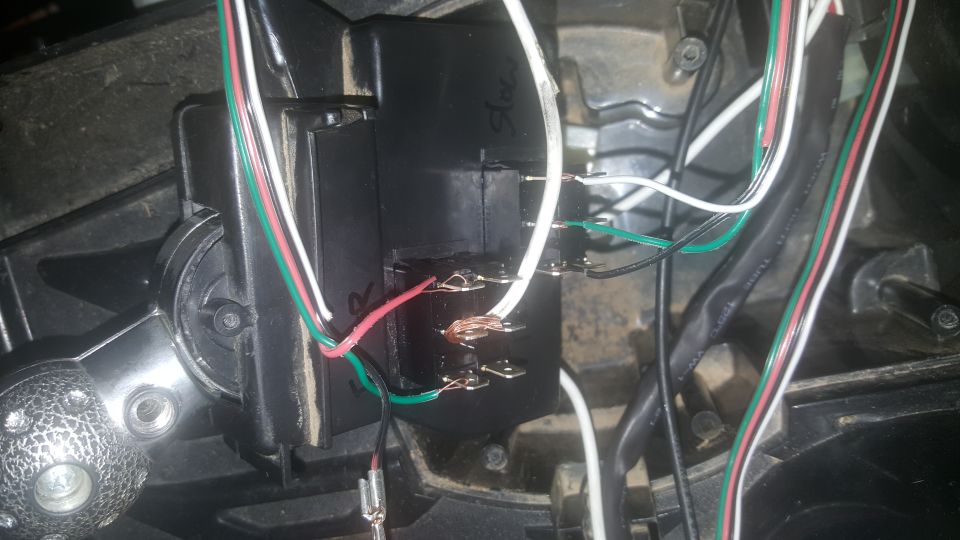 Close-up of a black electrical relay with multiple wires connected, some showing exposed copper. A silver textured knob is visible on the left