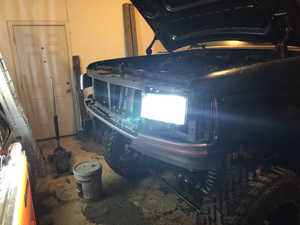 Black Ford truck with hood open, showing front grille and bright headlights. Modified suspension visible